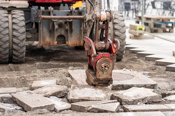 Detail of hydraulic jackhammer mounted on excavator arm working at old road reconstruction. Repairs in civil engineering.