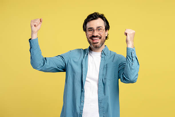 istock Excited man celebrating with raised fists on yellow background 2209941159
