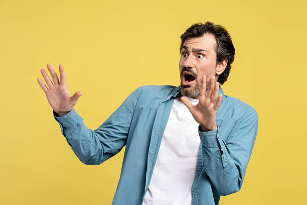 istock Scared man raising hands in fear on yellow background 2209941188