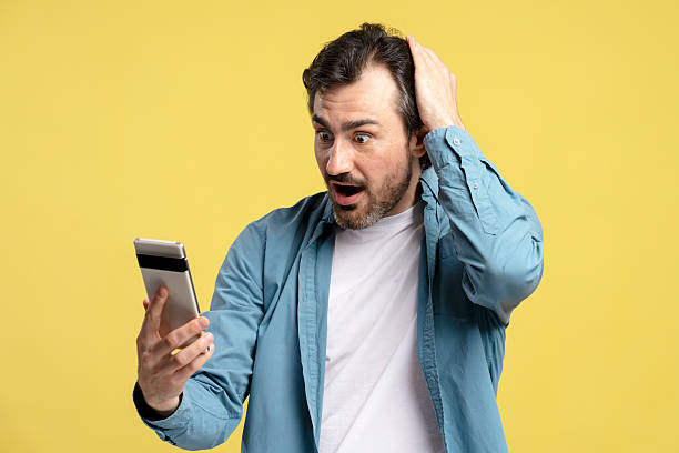 istock Shocked man reading unexpected news on smartphone on yellow background 2209941204