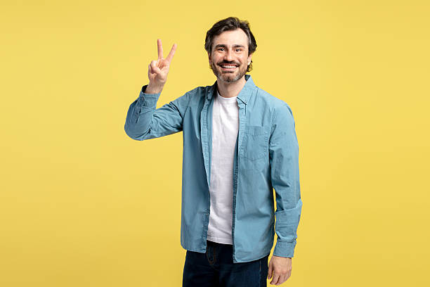 istock Smiling middle aged man showing victory sign on yellow background 2209941216