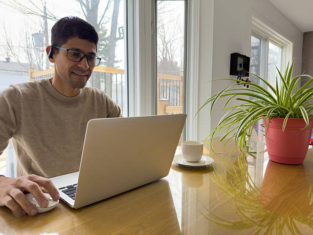 istock Man Working on Laptop at Kitchen Table with Coffee and Plant 2209941617