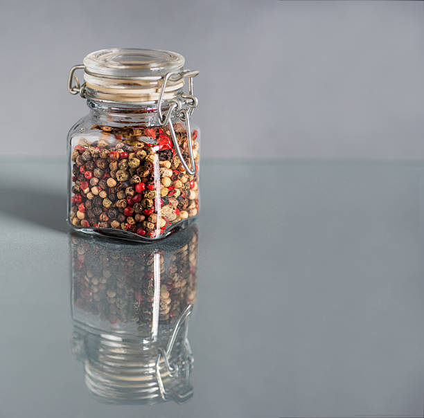 istock Glass jar with multicolored peppercorns on a glass table reflecting the jar, copy space. 2209943836