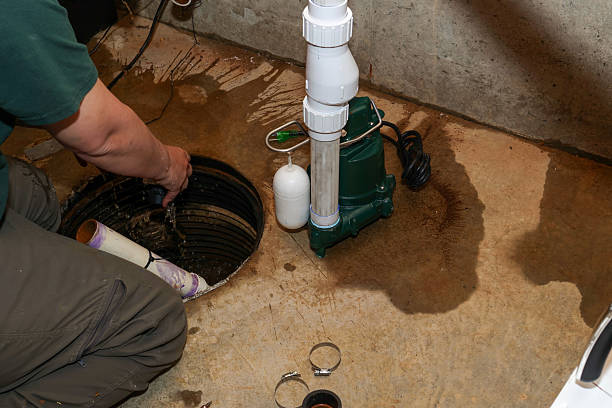 A plumber repairing a sump pump in a flooded basement in a residential home A plumber repairing a sump pump in a flooded basement in a residential home Water Removal or Flood Cleanup.