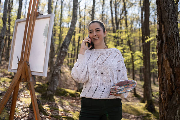 istock Woman Painting Outdoors While Talking on the Phone in a Forest Setting 2209951023