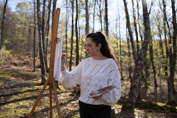 istock Young Woman Painting on Canvas Outdoors in a Lush Forest Setting 2209951084
