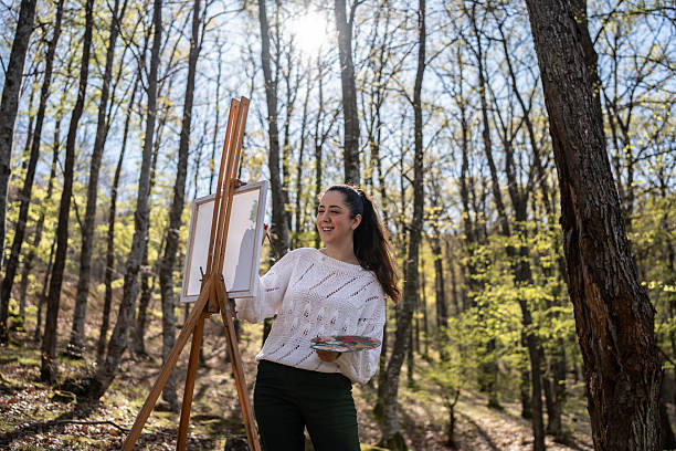 istock Woman Painting on an Easel in a Serene Forest Setting 2209951086