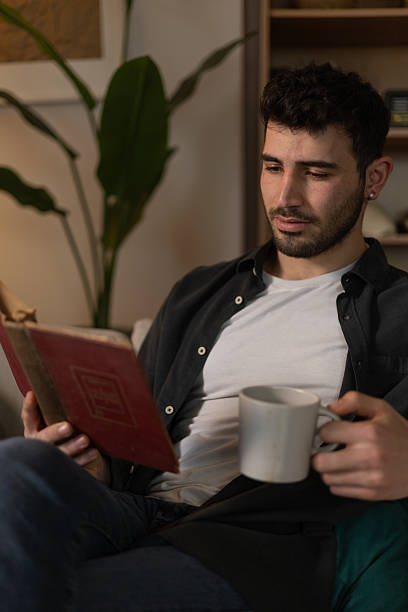 istock Young man enjoying a quiet moment at home, reading a book and drinking tea on his sofa 2209961403