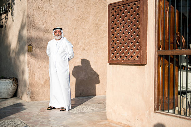 istock Senior Emirati Man in Traditional White Attire Standing by Rustic Architecture in Sunlight 2209969617