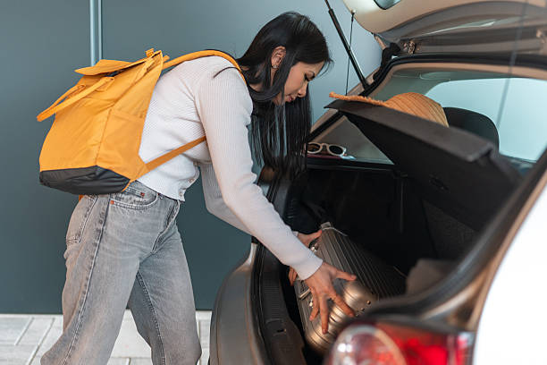 istock Young Asian Female Loading Suitcase Into Car Trunk Wearing Casual Attire in Daylight 2209969961