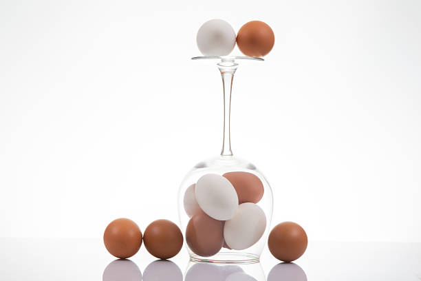 istock Surreal still life of a wine glass holding white and brown eggs, with three additional eggs nearby on a reflective white surface, blending simplicity and creativity 2209987118