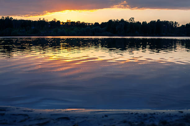 istock Serene lake at sunset with golden reflections on calm water, surrounded by lush trees under a dramatic sky. Perfect for nature and tranquility themes. 2209987947