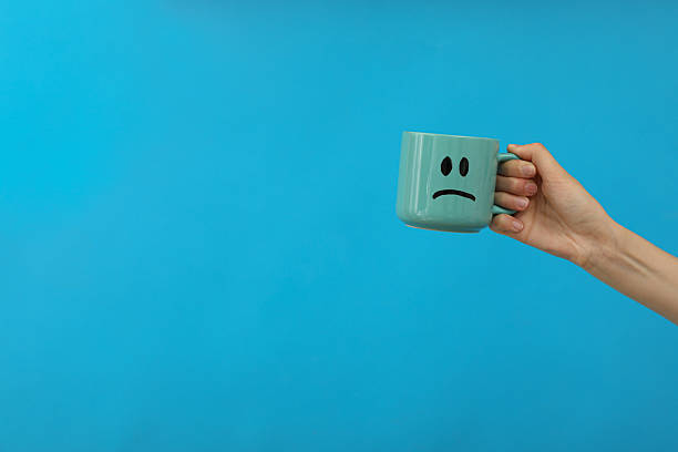 istock Cup with sad emoji in hand on blue background, space for text 2209992353