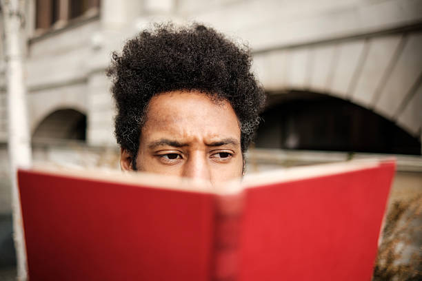 Serious young European man reads a book in red cover, close-up photo with selective soft focus and vintage tonal correction filter
