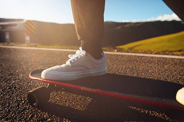 A close-up image focusing on a person's foot wearing a gray sneaker stepping on a skateboard on a red running track with blurred background