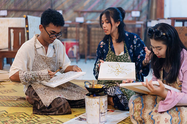 A group of diverse friends participate in a traditional batik workshop in Indonesia, drawing intricate wax patterns on fabric using a canting tool and hot wax. Seated on woven mats, they share space and conversation while honoring a centuries-old textile tradition rooted in cultural heritage and slow craftsmanship.