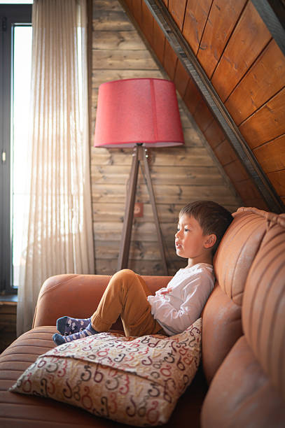 istock Young boy sitting on sofa gazing thoughtfully ahead 2210010615
