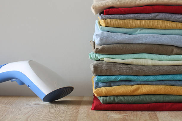 istock Steamer and stack of folded clothes resting on wooden table 2210011118