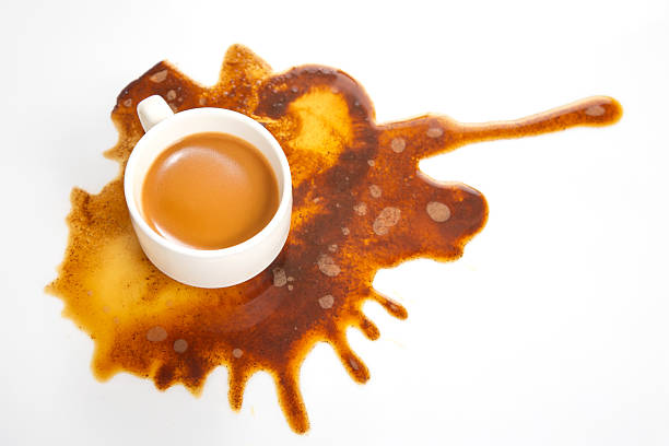 Rich coffee spills from a white cup, spreading across a pristine surface in a striking brown pattern, ideal for food and lifestyle themes
