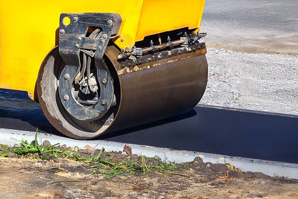 istock Close-up of a yellow road roller compacting fresh black asphalt on a construction site. The machine's large drum and wheel are visible, with gravel and grass on the side. 2210011993