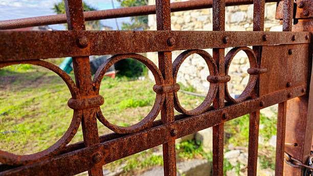 istock Close-up of a rusted iron gate with circular patterns, showing texture and wear against a garden and stone wall background. 2210012880