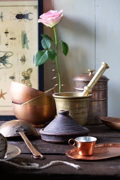 Rustic still life with antique kitchen tools, copper pots, and a single rose on a wooden table. Vintage cooking and nostalgic kitchen decor.