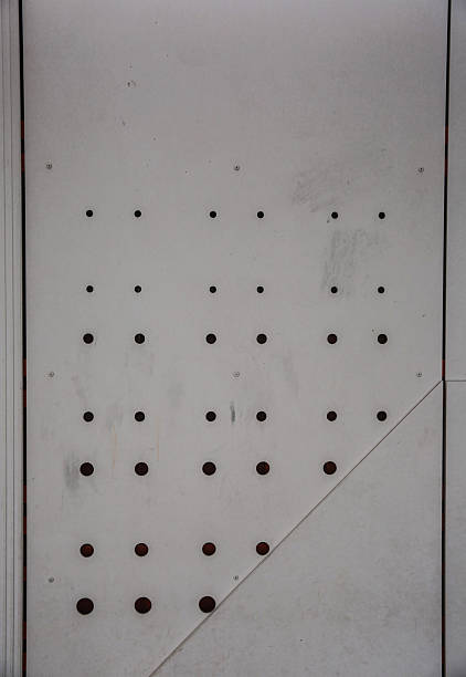 A close-up view of a minimalist metal wall panel featuring a pattern of small circular cutouts. The structured and geometrical design adds a contemporary and sleek aesthetic, perfect for modern architectural themes.