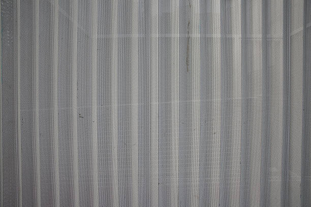 Detailed view of a metallic mesh exhibiting vertical lines under well-lit conditions, creating a clean and industrial aesthetic.