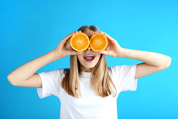 istock Young smiling girl with orange fruit on blue background 2210029755