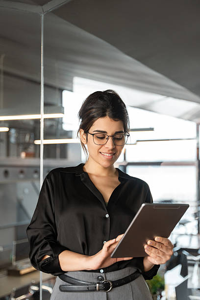 istock Young indian or arabian arab woman ceo manager holding digital computer tab for business project. Middle eastern or latin businesswoman using tablet pc online app for work standing in office. Vertical 2210031454