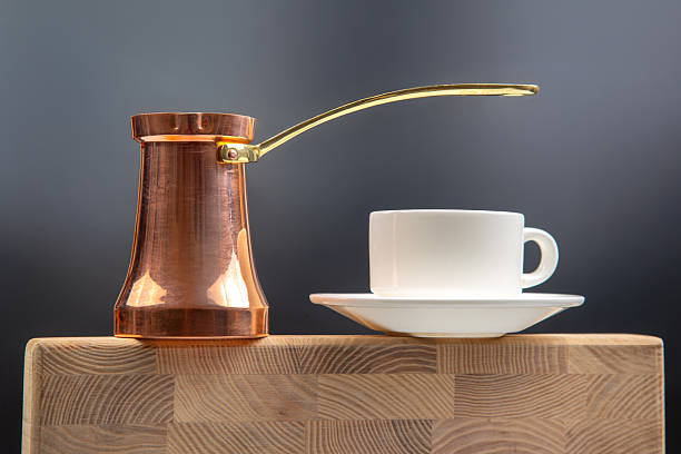 istock A shiny copper Turkish coffee pot with a brass handle beside a white ceramic cup and saucer, balanced on a wooden cutting board against a dark background, perfect for coffee culture photography 2210031571