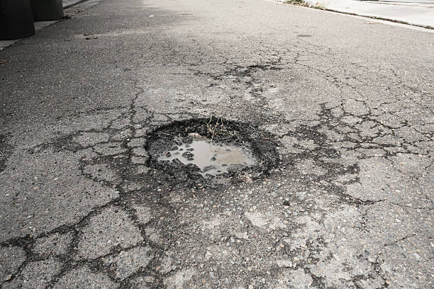 istock Cracks and pot hole in an old road 2210033479