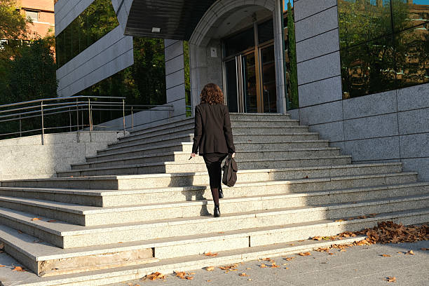 istock Executive woman from behind climbing stairs to enter modern office building 2210033807