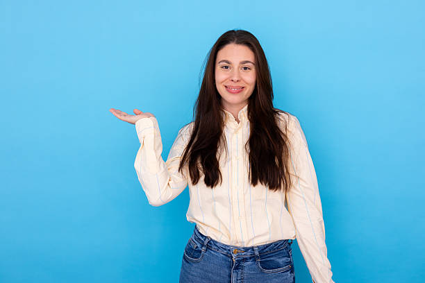 istock Young woman showing and presenting with open hand palm on blue background, looking at camera and smiling 2210038026