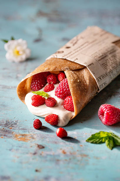 Vegan wrap filled with fresh raspberries and strawberries on light rustic background. Summer snack idea.