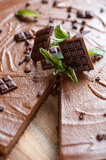 Overhead view of a round vegan chocolate mousse cake topped with dark chocolate pieces and fresh mint. Rustic background.