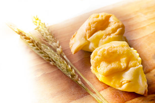 Abruzzo, Italy: fiadoni, a typical Easter speciality, with ears of wheat on a wooden table. Fiadoni are traditional savory pastries from the Abruzzo region of Italy. They’re like little cheese pies, traditionally made for Easter. The ingredients are flour, eggs, oil for the pastry, with a filling made with eggs, sharp Pecorino or other aged local cheese and sometimes  ricotta for a softer texture. In Abruzzo, fiadoni are a big part of Easter food traditions and often made in big batches to share.