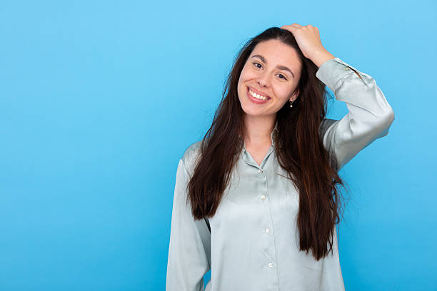 istock Professional female executive touching hair, smiling confidently against blue backdrop 2210040377