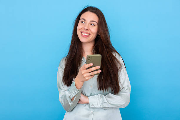 istock Young woman looking away while using smartphone and smiling on a blue background 2210041319