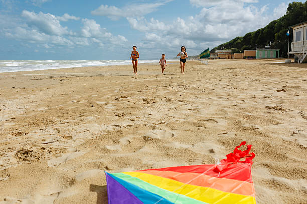 low angle view of three kids running together to take rainbow kite lying on the beach