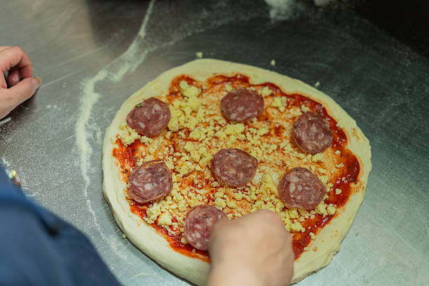 The owner of a Latin pizzeria in Bogota, Colombia, between 20 and 29 years old, prepares a pizza in the kitchen using ingredients such as sauces, flour