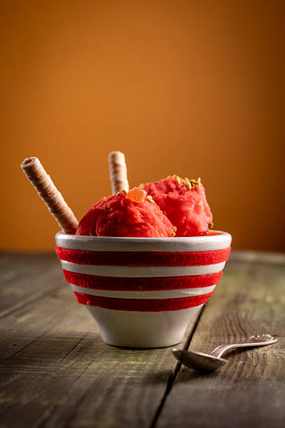 Strawberry gelato in striped bowl with wafers on rustic wooden table