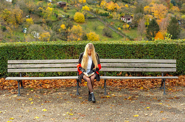 Blonde woman reading a book in the park on a wooden bench on a sunny day in autumn