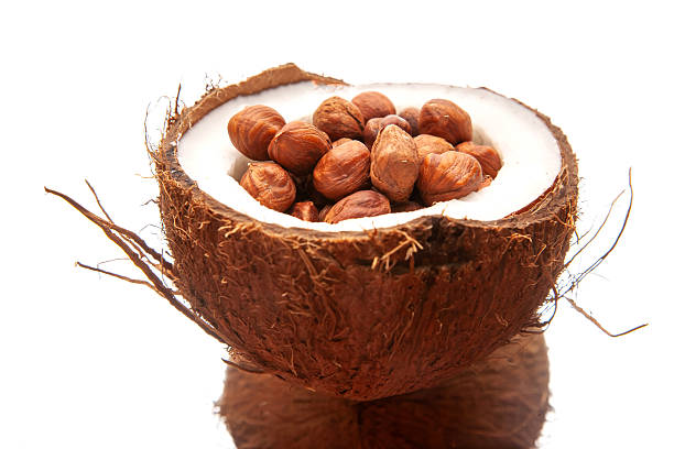 Close-up of a split coconut packed with hazelnuts, set against a clean white backdrop. Ideal for natural food visuals, tropical snack promotions, or creative culinary photography