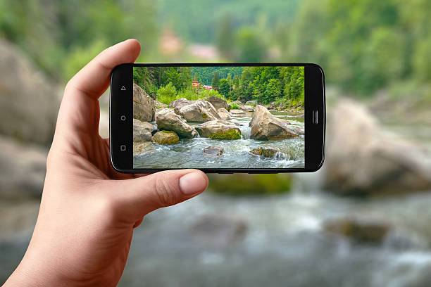 Smartphone in hand photographs nature on the screen. Photos of the mountain river for posting on social networks
