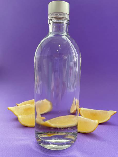 istock Clear glass bottle with lemon slices on purple background 2210056754