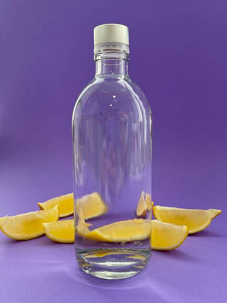 Transparent glass bottle with lemons on purple background
