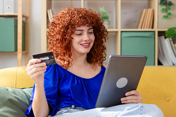 istock Smiling young woman using digital tablet and credit card on sofa at home 2210070752
