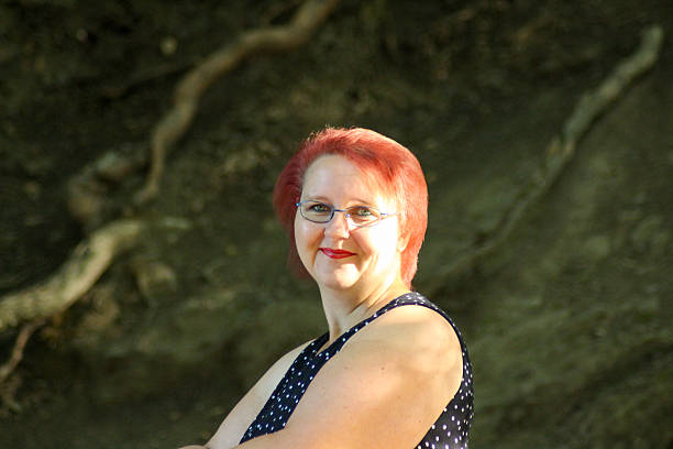 Red-haired woman with bright blue eyes stands on a bridge in summer light