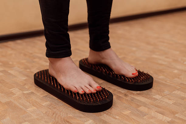 istock Women's feet on nails. A woman's legs. Sadhu Board Therapy 2210079153